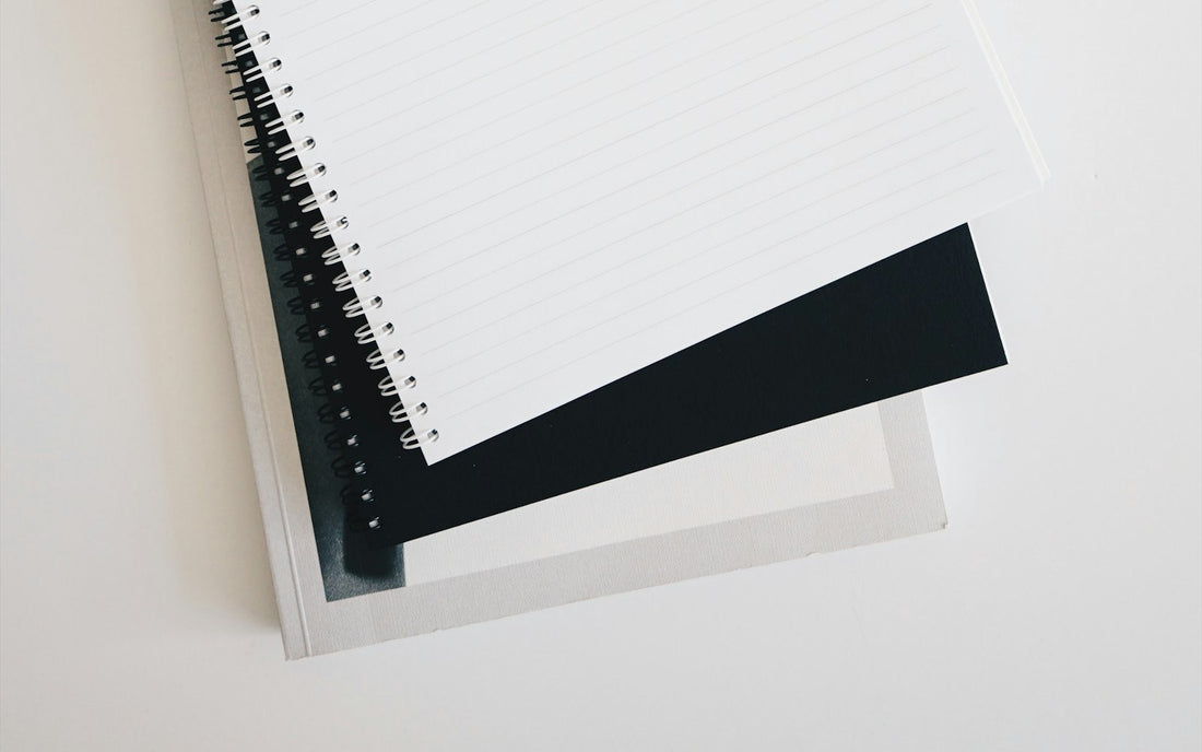 Minimal white desk with a spiral notebook, pen and keyboard