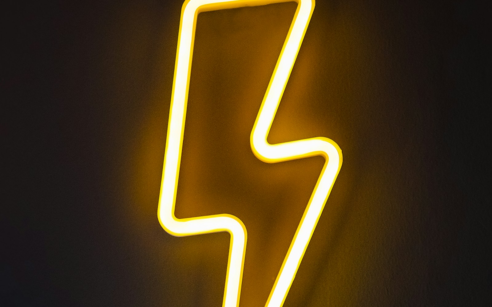 Glowing yellow neon lightning bolt on a dark wall